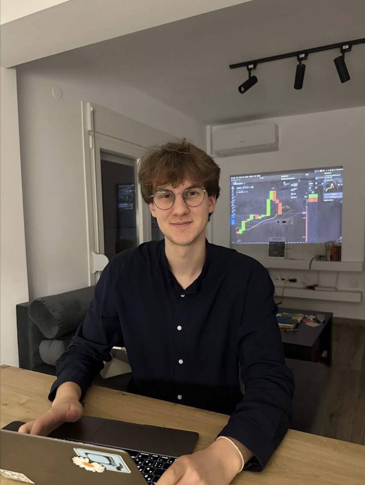 Oliver at a laptop, with a financial chart on a monitor behind him